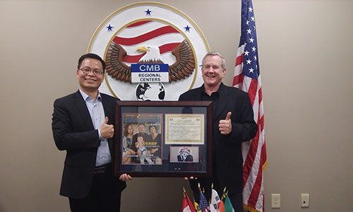 美成達小邱總（邱少波先生）接受CMB總裁Patrick F.Hogan先生贈送帶有陳先生一家采訪照片的雜志以及頒發給美成達的榮譽證書